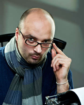 Old fashioned bald writer in glasses writing book on a vintage typewriter