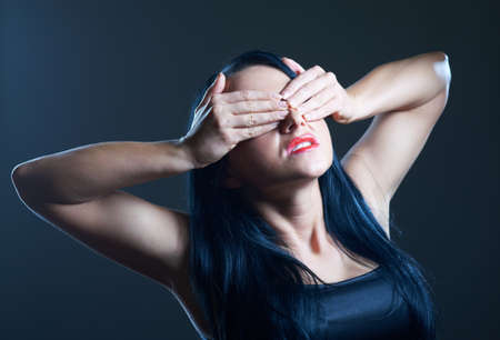 Portrait of young woman in darkness covering her eyesの写真素材