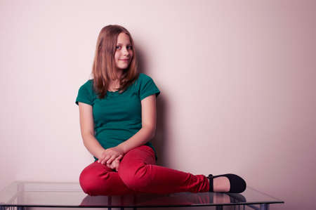 Portrait of a teen girl sitting on table, studio shotの写真素材