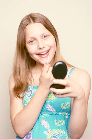 Happy teen girl holding mirror, looking at the camera and colors lipsの写真素材
