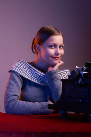 Cute happy teen girl sitting at table with typewriterの写真素材