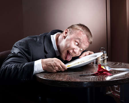 Muscular businessman eating and lick the plateの写真素材