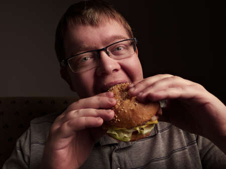 Lonely fat guy eating hamburger. Bad eating habits. Closeup.の写真素材