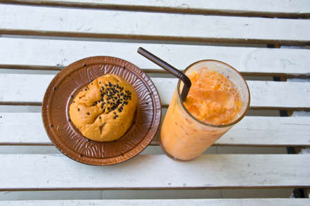 Refreshing cold Thai milk Iced Tea and bread on tableの写真素材