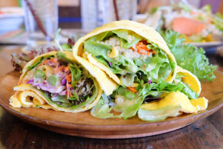 Egg wrap with salad and fresh vegetables on a wooden plate, cut in halfの写真素材