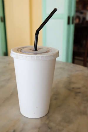 Disposable cup for beverages with straw on tableの写真素材