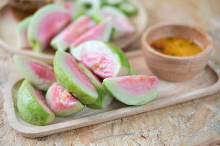 Ripe guava fruit cut with sweet sauce, Thai food on wood tray. Selective focusの写真素材
