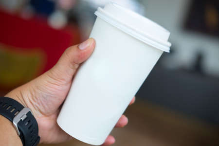 man's hand holding white empty paper coffee cup with a plastic cap