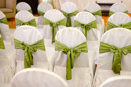Chairs for a party with green covers ribbon and bow. Shallow depth of field with the first chair in focusの写真素材