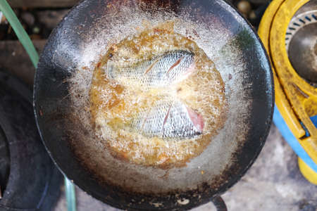 Fried tilapia fish in a frying pan with hot oilの写真素材