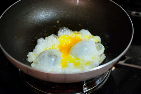 Fresh egg in hot oil on black cooker in kitchenの写真素材