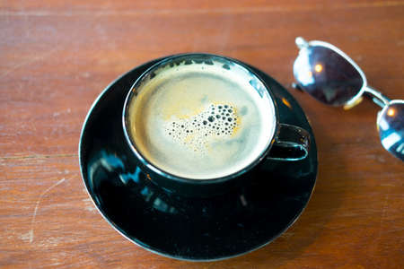 Hot coffee in black cup with sunglasses on tableの写真素材