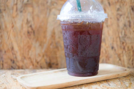 Take away plastic cup of iced black coffee americano on wooden table in a coffee shopの写真素材
