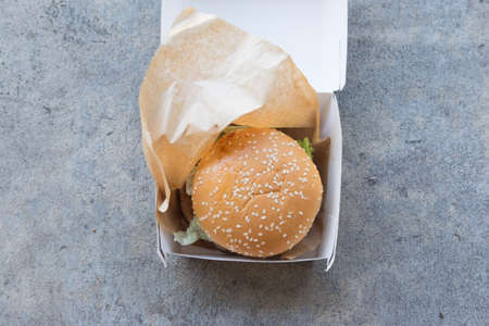 Hamburger is a fast food make from bun meat cheese and vegetable in white paper boxの写真素材