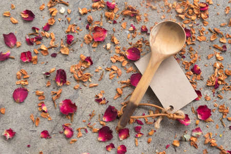 Close up wood spoon and paper tag on dry petals roses backgroundの写真素材