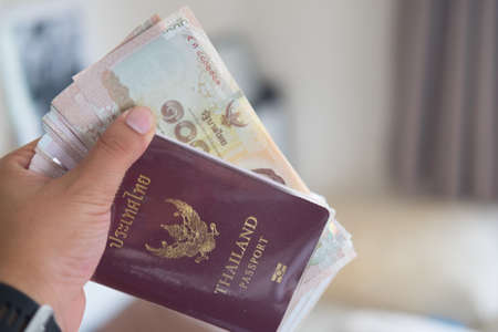 Man hand of a man checking Thailand passports with Thai money