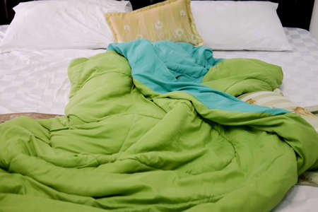 Green duvet and whie pillows on an unmade bed