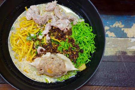 Tom Yum Kung with yellow and green noodles and seafood in black bowlの写真素材