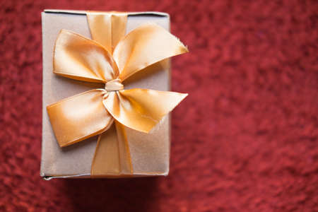 Brown gift box with golden ribbon on red backgroundの写真素材