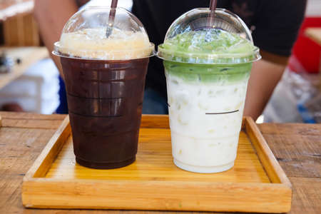 Two plastic take away cup of iced black coffee americano and iced green tea latte on wood table in coffee shopの写真素材