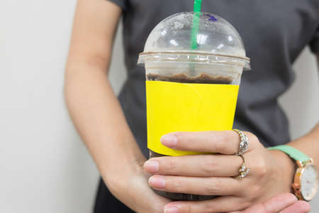 Young woman is drinking coffee, Close up of hands with yellow take away cup of coffeeの写真素材