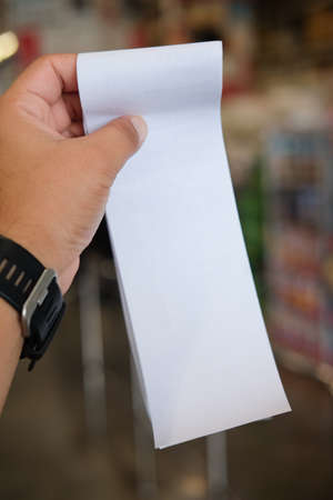 Hand holding paper receipt or receiving billing invoice with total expense (Supermarket shop)の写真素材