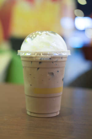 Chocolate frappe with whipped cream in plastic glass on wooden table in a cafe