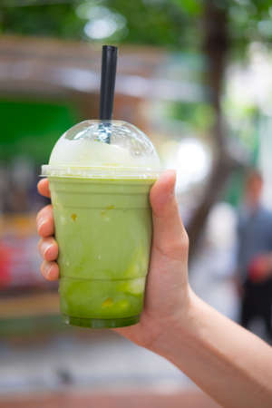 hand holding cup of Japanese matcha green tea ice smoothie frappe with cream toningの写真素材
