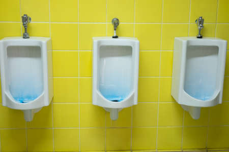 Urinal in men bathroom white ceramic with yellow tile background
