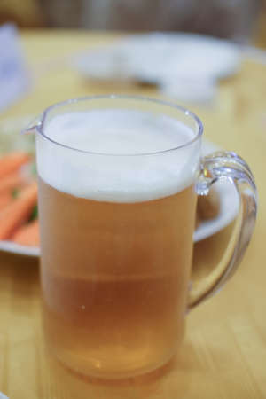 Big mug of beer standing on dinner table with food  backgroundの写真素材