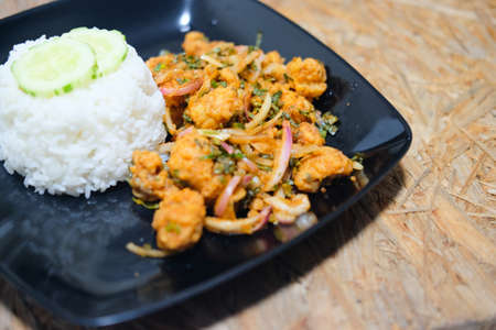 Spicy salad fried chicken with rice in black dish on wooden table, Thai foodの写真素材