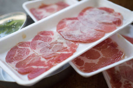 Thin sliced pork meat in white plate prepared for shabu or sukiyaki hot potの写真素材