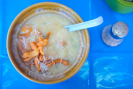 Congee rice porridge in yellow bowl, top view.
