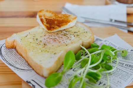 Egg fried in a hole of a slice of bread served with vegetable on a wooden plate.の写真素材