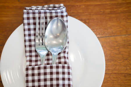 Spoon and fork with napkin setting on wood table top view
