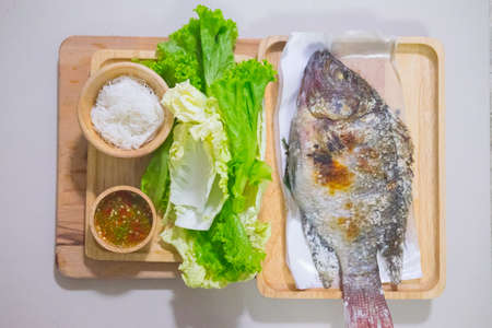 Tilapia fish grilled with salt in wood dish and have spicy sauce, Thai foods style placed on wooden table.の写真素材