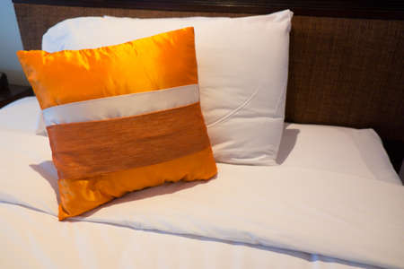 Decorative orange silk pillows on white bedの写真素材