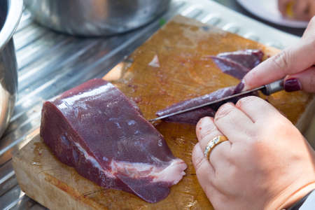 Chef slices raw liver on a cutting boardの写真素材