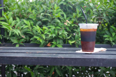 A glass of iced black coffee on the wooden table in the garden.