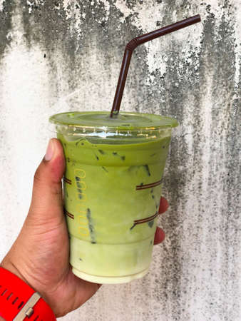Hand holding ice milk green tea with cement background, summer drink