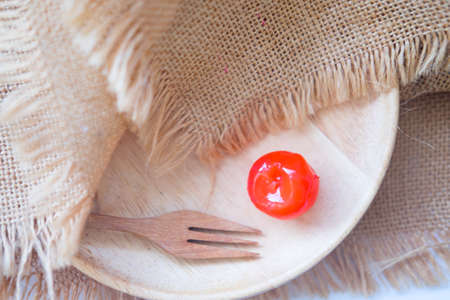 One red cherry on wooden dish, top view