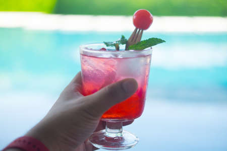 Fresh drink punch juice with ice, cherry and mint in young hand at the party