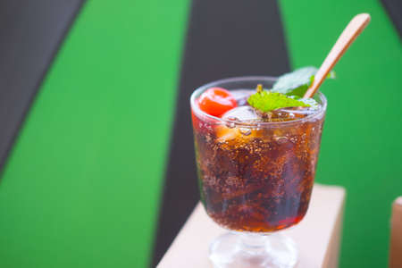 Glass of soft drink with cherry and mint on black and green background