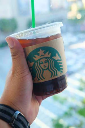 Thailand Dec 18 2017 : Male hand holding Starbucks takeaway iced coffee cup outdoors on the street displaying the green logoのeditorial素材
