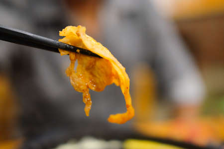 Hand holding chopstick with grilled korean pork grilled yakiniku japanese style.の写真素材