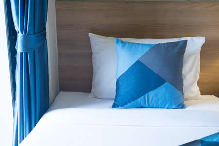 Blue and white pillows on sheets bed with blue curtain. Vacation concept with hotel apartment...