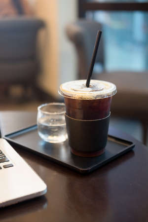 Iced black coffee with notebook on wood table
