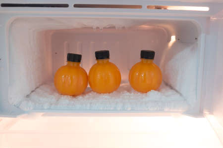 Open fridge filled with orange juice bottles (three bottles)