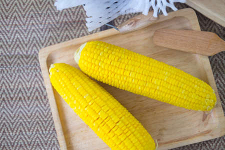 Boiled yellow ripe whole corn on wooden tray