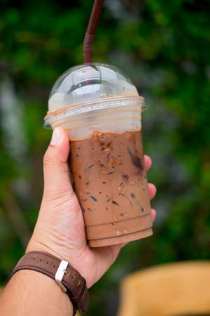 Hand holding a glass iced mocha in nature background